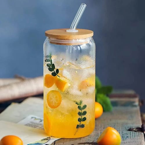 Glass jar with a wooden lid and straw filled with iced lemonade and garnished with lemon slices and mint leaves on a blue background.